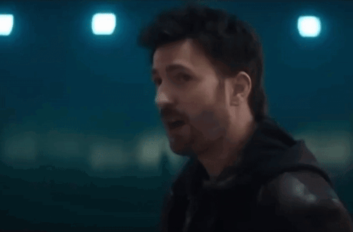 A Man With A Beard Is Talking To Another Man In A Dark Room . GIF