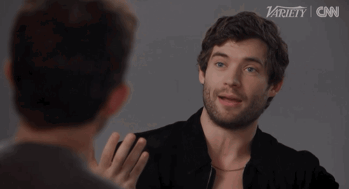 A Man With A Beard Is Talking To Another Man In Front Of A Variety Logo GIF