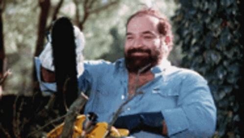 A Man With A Beard Is Using A Chainsaw To Cut A Tree Branch GIF