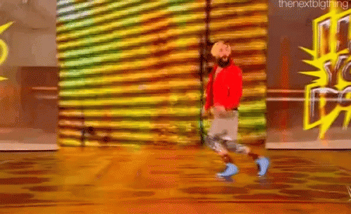 a man with a beard is walking on a wooden floor in front of a wall with graffiti on it .