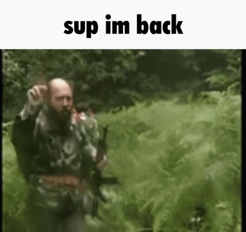 A Man With A Beard Is Walking Through A Field With The Words " Sup Im Back " At The Top GIF