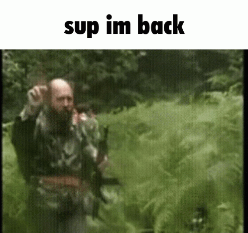 A Man With A Beard Is Walking Through A Grassy Field With The Words " Sup Im Back " Above Him GIF