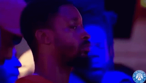 A Man With A Beard Is Watching A Basketball Game In A Dark Room With Blue Lights . GIF