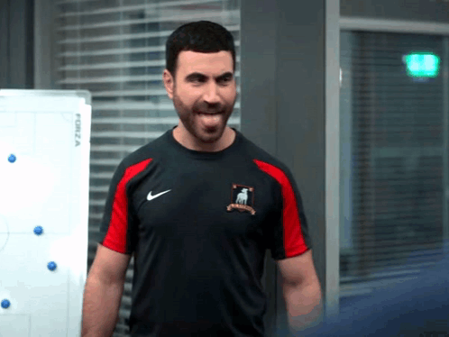 A Man With A Beard Is Wearing A Black And Red Nike Shirt . GIF