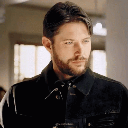 A Man With A Beard Is Wearing A Black Jacket And Looking At Something . GIF