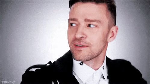 A Man With A Beard Is Wearing A Black Jacket And White Shirt And Making A Funny Face . GIF