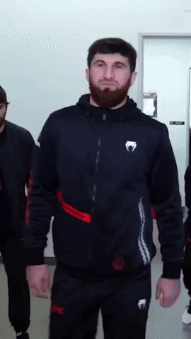 A Man With A Beard Is Wearing A Black Jacket With A White Venum Logo On The Front GIF