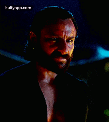 A Man With A Beard Is Wearing A Black Shirt And Looking At The Camera . GIF