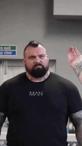 A Man With A Beard Is Wearing A Black Shirt That Says Man On It GIF