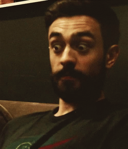 A Man With A Beard Is Wearing A Black Shirt With A Green Circle On It GIF
