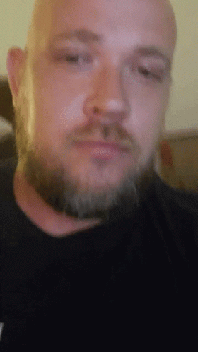 A Man With A Beard Is Wearing A Black Shirt With A T On It GIF