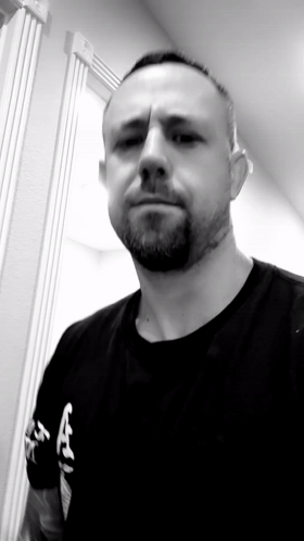 A Man With A Beard Is Wearing A Black Shirt With The Letter A On The Front GIF