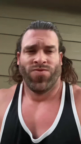 A Man With A Beard Is Wearing A Black Tank Top And Making A Funny Face GIF