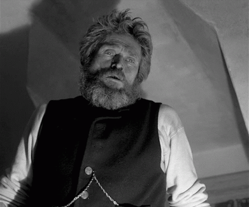 A Man With A Beard Is Wearing A Black Vest And A Chain Around His Neck GIF