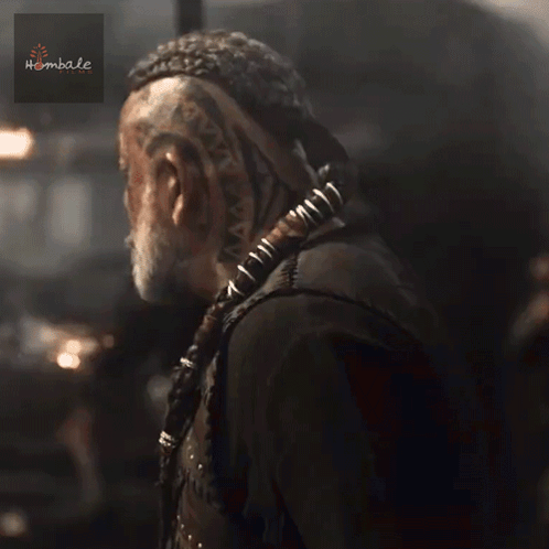 A Man With A Beard Is Wearing A Black Vest With Studs And A Sticker That Says Hembale GIF