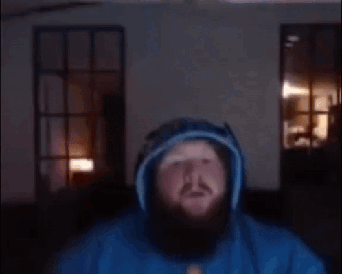 A Man With A Beard Is Wearing A Blue Hoodie And Headphones And Giving A Thumbs Up . GIF