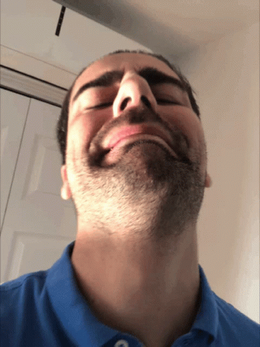 A Man With A Beard Is Wearing A Blue Shirt And Making A Funny Face GIF