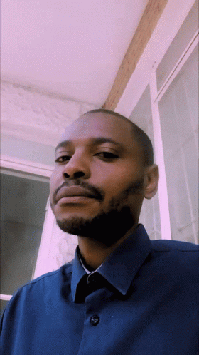 A Man With A Beard Is Wearing A Blue Shirt With Buttons On The Front GIF
