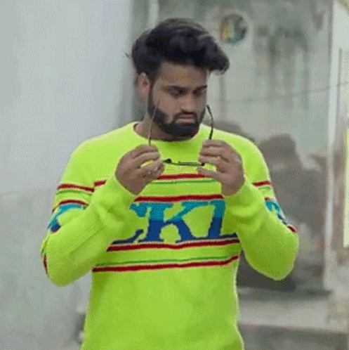 A Man With A Beard Is Wearing A Bright Yellow Sweater And Holding Glasses . GIF