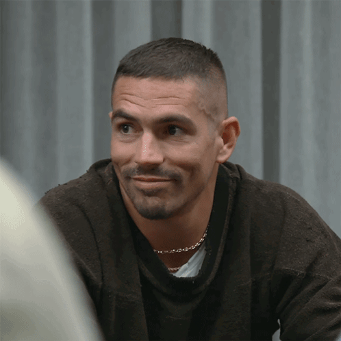 A Man With A Beard Is Wearing A Brown Sweater And A Gold Chain Around His Neck GIF