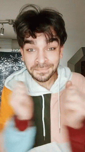 A Man With A Beard Is Wearing A Colorful Hoodie And Giving A Thumbs Up Sign GIF
