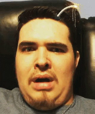 A Man With A Beard Is Wearing A Gray Shirt And A Necklace GIF