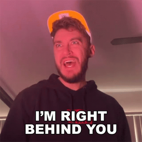 a man with a beard is wearing a hat and a hoodie and says i 'm right behind you .