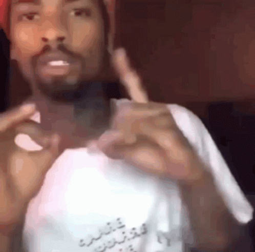 A Man With A Beard Is Wearing A Hat And A White Shirt And Making A Funny Face . GIF