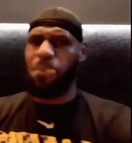 A Man With A Beard Is Wearing A Hat And Sunglasses While Sitting On A Couch . GIF