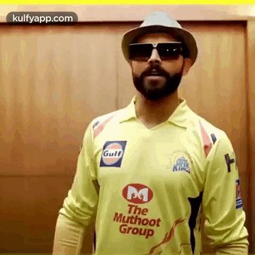 A Man With A Beard Is Wearing A Hat And Sunglasses While Wearing A Yellow Shirt . GIF