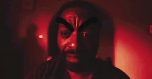 A Man With A Beard Is Wearing A Mask With A Cross On His Face GIF