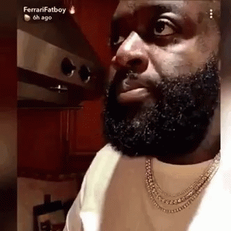 A Man With A Beard Is Wearing A Necklace And Looking At The Camera . GIF