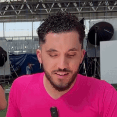 A Man With A Beard Is Wearing A Pink Shirt And Smiling While Holding A Microphone . GIF