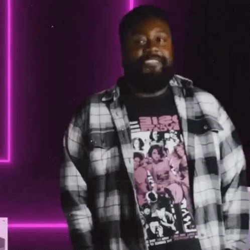 A Man With A Beard Is Wearing A Plaid Shirt And A Black Shirt GIF