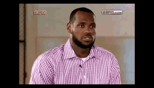 a man with a beard is wearing a purple and white striped shirt and talking to a microphone .