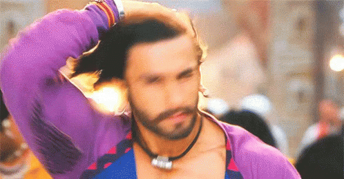 A Man With A Beard Is Wearing A Purple Shirt And A Necklace . GIF