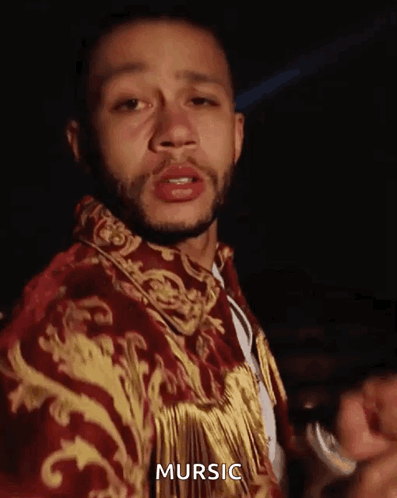 a man with a beard is wearing a red and gold jacket with the word mursic on it .