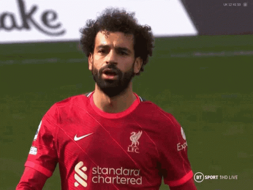 A Man With A Beard Is Wearing A Red Jersey That Says Standard Chartered GIF