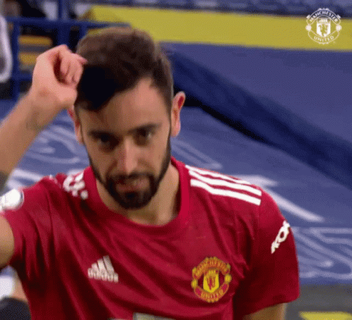 A Man With A Beard Is Wearing A Red Manchester United Jersey And Adjusting His Hair . GIF