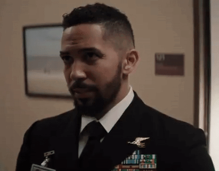 A Man With A Beard Is Wearing A Suit And Tie And Standing In A Hallway . GIF