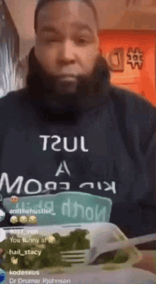 A Man With A Beard Is Wearing A T2ul Hoodie And Holding A Plate Of Food . GIF