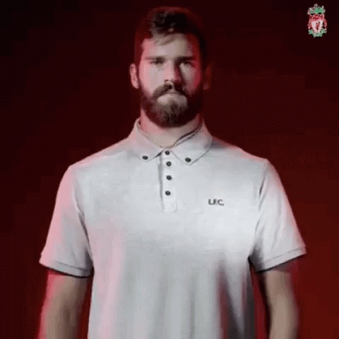 A Man With A Beard Is Wearing A White Polo Shirt And Standing In Front Of A Red Background . GIF