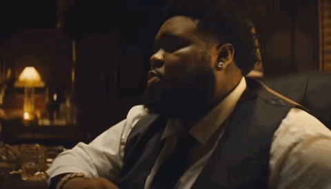 A Man With A Beard Is Wearing A White Shirt And A Black Vest . GIF