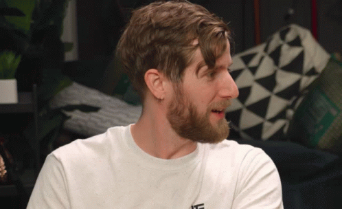 A Man With A Beard Is Wearing A White T-Shirt With The Letter L On The Front GIF