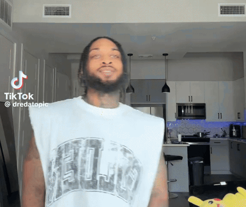 A Man With A Beard Is Wearing A White Tank Top That Says ' Chicago ' On It GIF