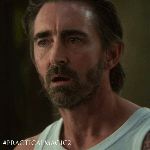 a man with a beard is wearing a white tank top with # practicalmagic2 written on it