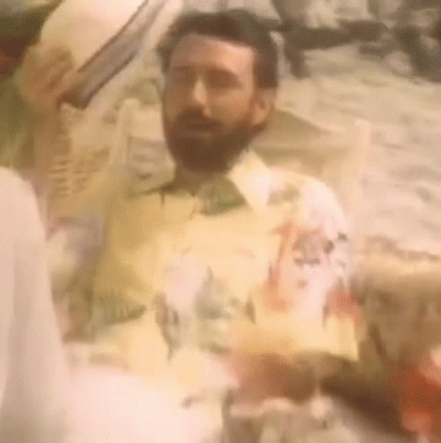 A Man With A Beard Is Wearing A Yellow Shirt And A Hat GIF