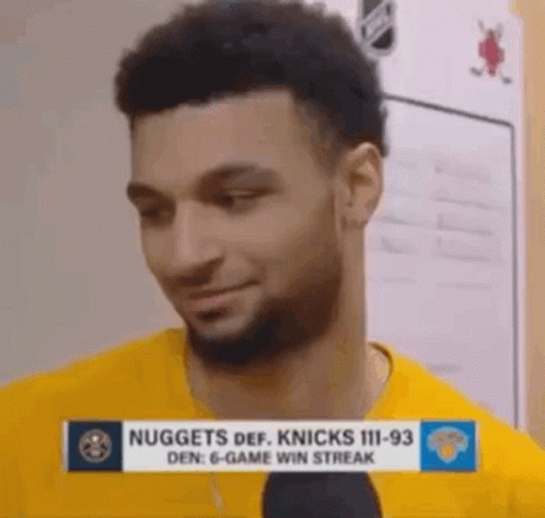 A Man With A Beard Is Wearing A Yellow Shirt And Talking Into A Microphone In A Locker Room . GIF