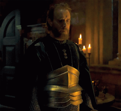 a man with a beard is wearing armor and standing in front of a window with candles
