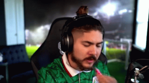 A Man With A Beard Is Wearing Headphones And A Green Shirt . GIF